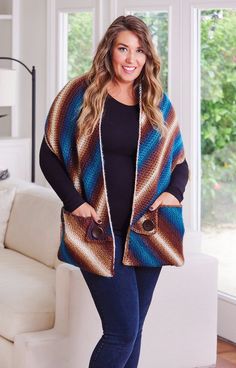 a woman standing in front of a couch wearing a blue and brown ponchle