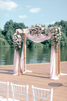 an outdoor ceremony setup with white chairs and flowers on the altar, along side water