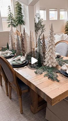 a dining room table decorated for christmas with pine trees and evergreens on the tables