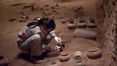 a woman kneeling down in front of clay pots