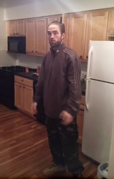 a man standing in a kitchen next to a white refrigerator freezer and wooden floors