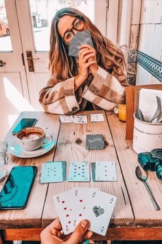 a woman sitting at a table with playing cards in front of her and drinking coffee