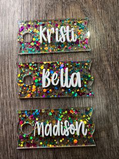 three name tags with confetti on them sitting on a wooden table, one says krisu beula madison