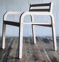 two white chairs sitting next to each other on top of a hard wood floor in front of a brick wall