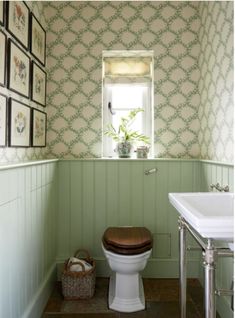 a bathroom with green and white wallpaper, wooden toilet seat, sink and window