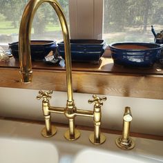 two brass faucets in front of a window with bowls on the windowsill