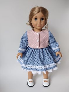 a doll with blonde hair wearing a blue dress and white polka dot print shoes, standing against a gray background