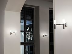 two lights are on the wall in front of a door with glass panels and metal handles