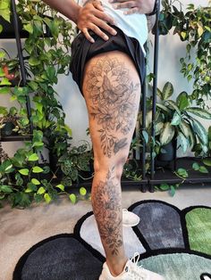 a woman with tattoos on her legs and leg is standing in front of a potted plant