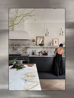 a woman in a black dress standing at a kitchen counter with an oven and sink