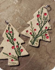 two ceramic christmas trees with red berries and green leaves on them, sitting on a stone surface