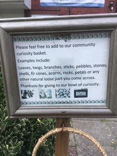 a sign on a pole in front of some bushes and trees with words written below it