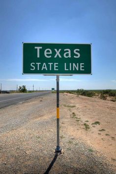 a green texas state line sign sitting on the side of a road next to a desert