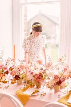 a woman standing in front of a table with flowers and candles on top of it