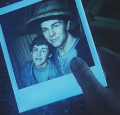 a person holding up a polaroid with a picture of two people on it in front of them