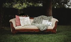 a couch sitting in the middle of a field with pillows on it's back