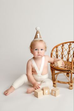 a baby sitting on the floor wearing a birthday hat with blocks in front of it