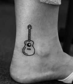 a black and white photo of a guitar tattoo on the ankle, which is also part of a foot