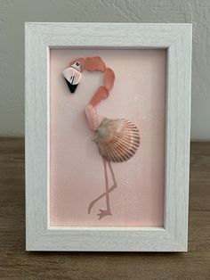 a pink and white frame with a sea shell in the shape of a flamingo