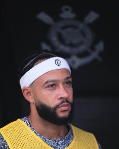 a man with a beard wearing a yellow shirt and white headband standing in front of a black background