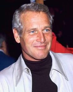 a close up of a person wearing a white jacket and black turtle neck sweater, smiling at the camera