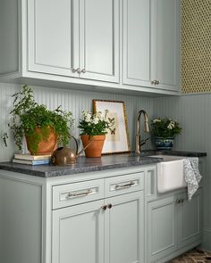 a kitchen with white cabinets and green plants on the counter top, next to a sink