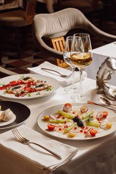 a table topped with plates of food next to glasses of wine and utensils