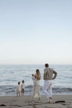 a man and two women walking on the beach with their children looking out at the ocean