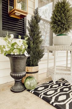 two potted plants sitting on the front porch next to a rug and window sill