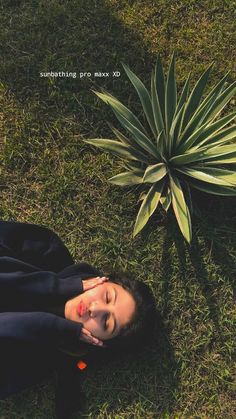 a woman laying on the ground next to a plant and looking up at her face