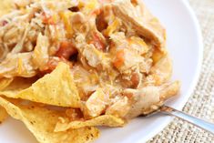 a white plate topped with nachos covered in chicken and salsa next to tortilla chips