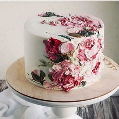 a white cake with pink flowers on it sitting on top of a wooden table next to a wall