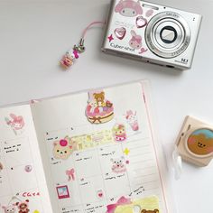 an open planner book with stickers and a camera on the table next to it