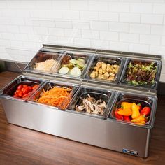 a stainless steel food tray filled with different types of salads and vegetables on top of a wooden table