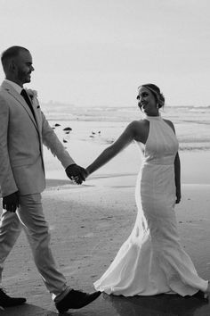 a bride and groom walking on the beach holding hands