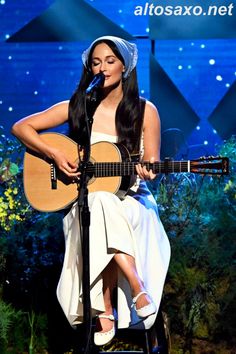 a woman sitting on top of a stool holding a guitar in front of a microphone