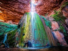 a waterfall with green moss growing on it's side in the middle of a canyon