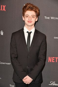 a young man in a suit and tie standing on a red carpet at an event