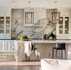 a large kitchen with marble counter tops and white cabinets, along with two bar stools