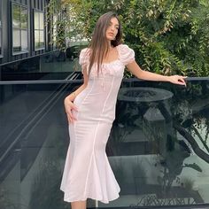 a woman in a white dress leaning against a glass wall and posing for the camera