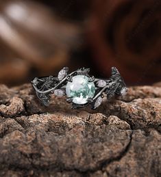 a ring with a green stone in the middle on top of some rocks and wood