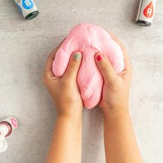 a person holding a pink doughnut in their hands with other items around them on the table