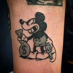 a mickey mouse tattoo on the leg of a person with money bags in front of him