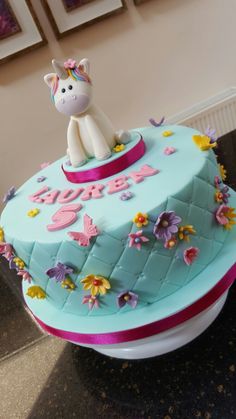 a birthday cake decorated with flowers and a unicorn figure on top is sitting on a table