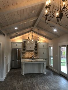 an empty kitchen with wood floors and white cabinets, chandelier hanging from the ceiling