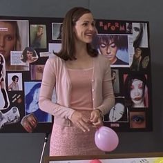 a woman standing in front of a table with balloons and pictures on the wall behind her