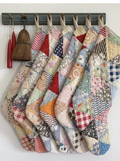 several pieces of colorful quilt hanging from hooks on a white wall next to brooms