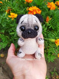 a small crocheted pug dog sitting on top of a persons hand in front of some flowers