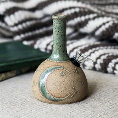 a small ceramic bottle sitting on top of a bed next to a book and blanket