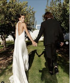 a bride and groom holding hands walking through the grass